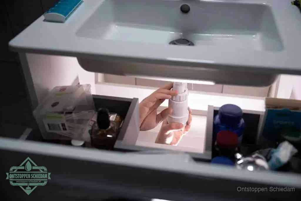 Een pompfles met zeep boven een wastafel, de heet water en afwasmiddel-methode om een vetprop in de afvoer los te maken in Schiedam