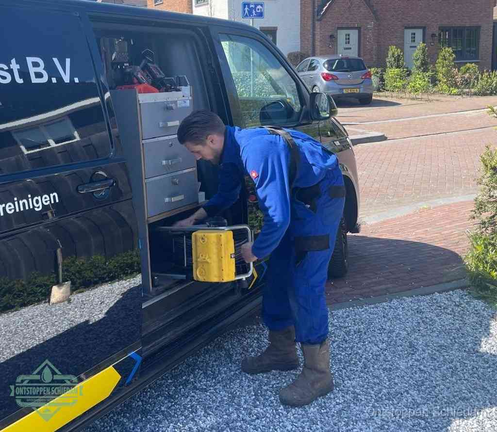 Een monteur pakt buiten op de oprit gereedschap uit de bedrijfsbus, het moment om een professional in te schakelen voor een verstopte afvoer in Schiedam