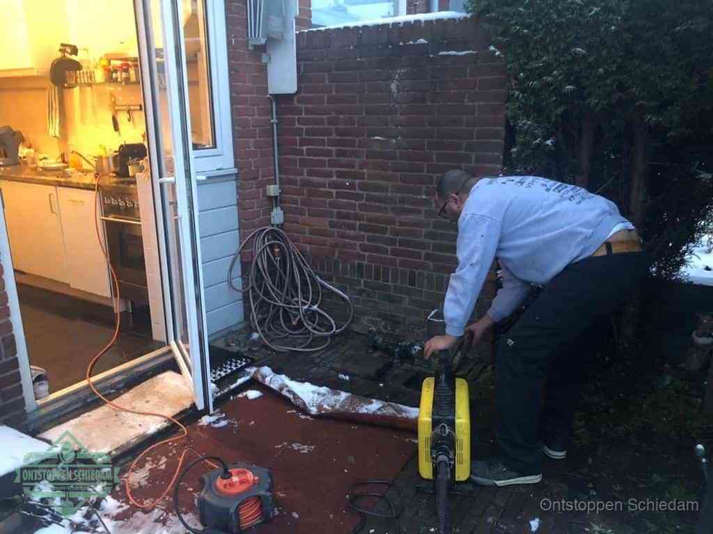 Een monteur werkt buiten bij een open riool-/grondput met een elektrische ontstoppingsmachine om een verborgen afvoerprobleem op te sporen in Schiedam
