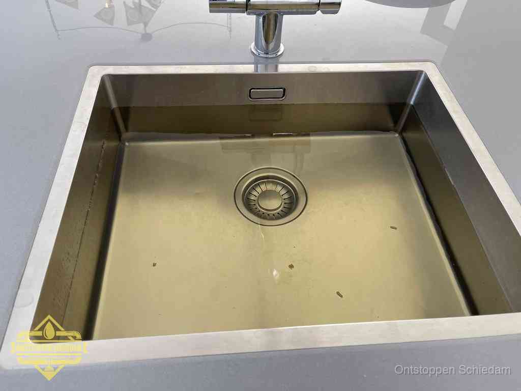 Stilstaand water in een rvs spoelbak dat niet wegloopt, een duidelijk signaal van een gootsteenverstopping in Schiedam