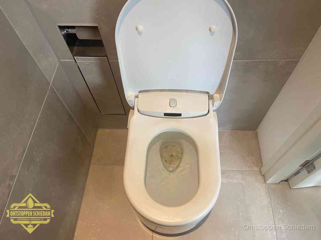 Een wit hangtoilet waarin een prop wc-papier op het water blijft drijven, een duidelijk signaal van een verstopte wc in Schiedam
