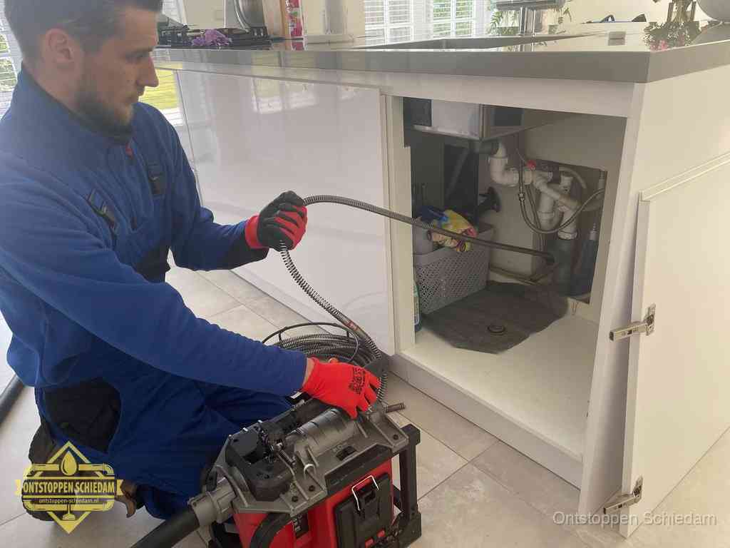 Een monteur reinigt de keukenafvoer grondig met een veermachine om terugkerende gootsteenverstoppingen te voorkomen in Schiedam