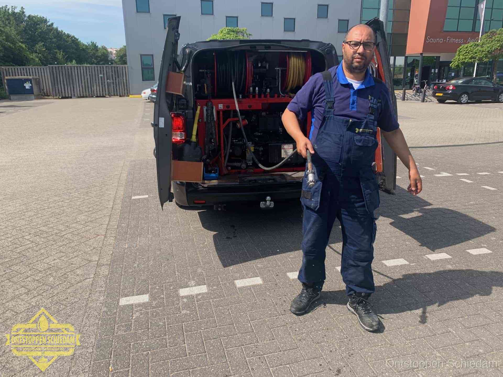Een monteur bij zijn bestelbus met een hogedruk- en rioolreinigingsunit, klaar om de oorzaak van terugkerende wc-verstoppingen aan te pakken in Schiedam