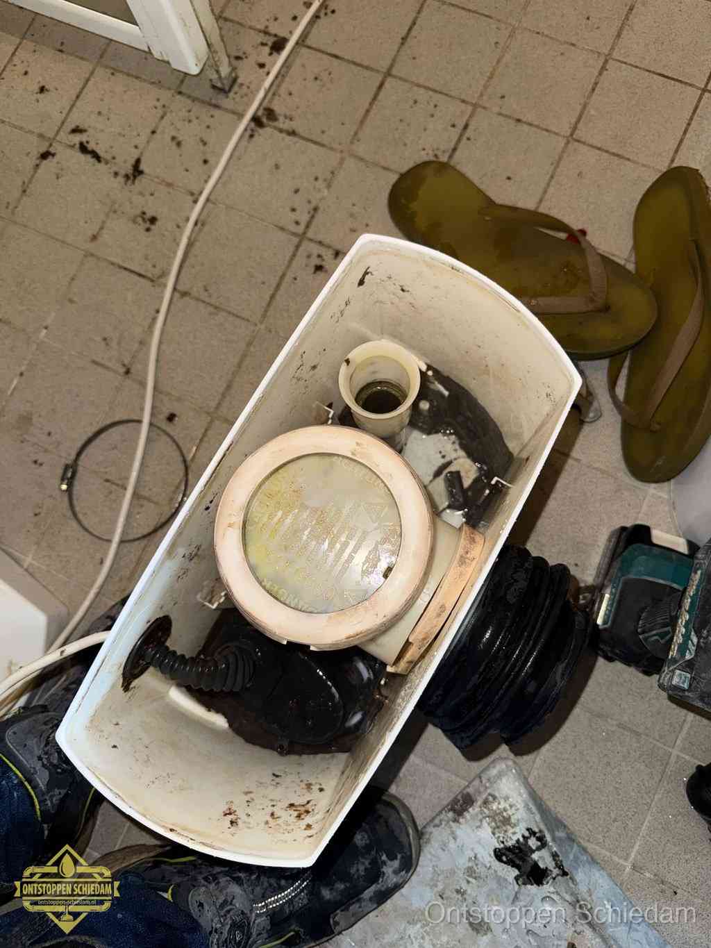 Een gedemonteerde toiletpot op de vloer met ontstoppingsveer en gereedschap ernaast, het verwijderen van een vastzittend voorwerp uit de wc in Schiedam