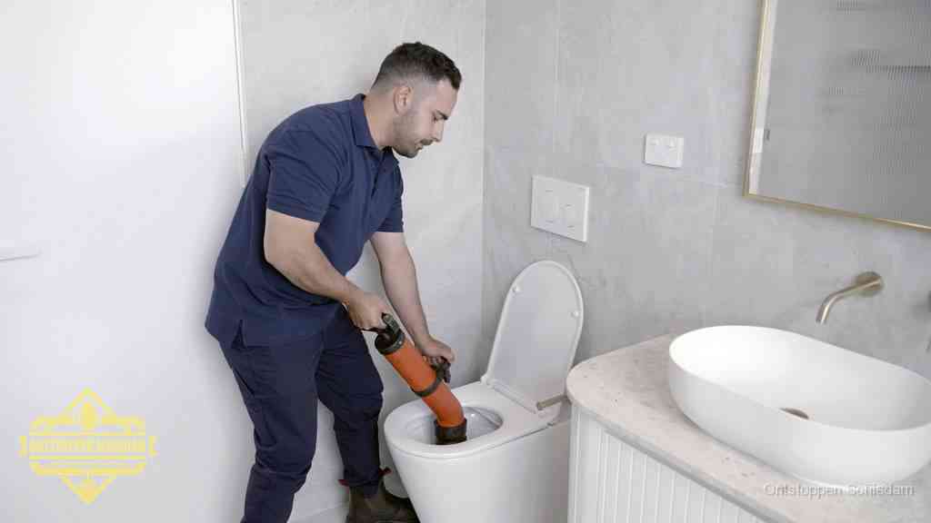 Een man gebruikt een handmatige luchtdruk-ontstopper in een modern betegeld toilet om zelf de wc te ontstoppen in Schiedam